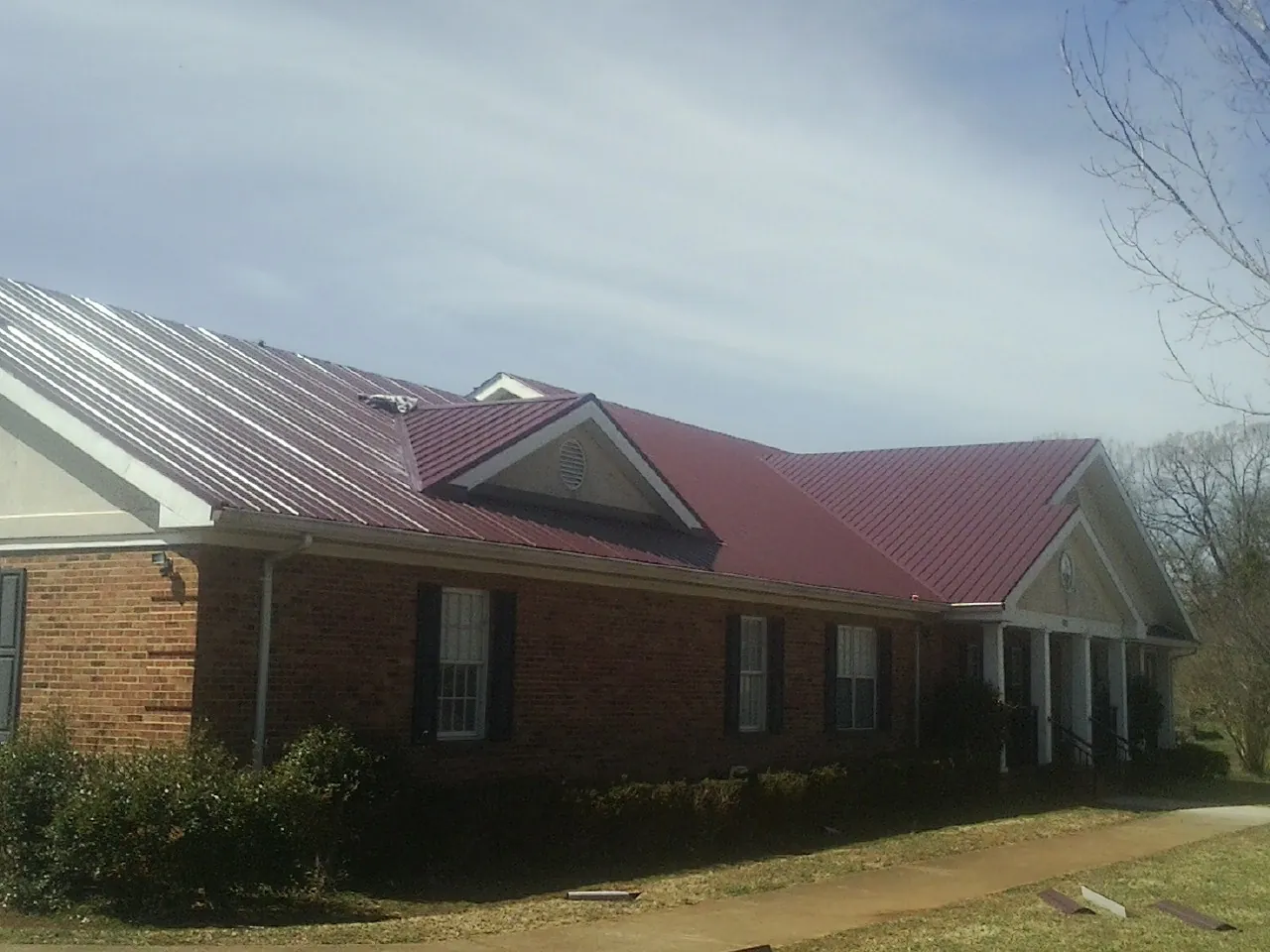 Red metal roof with gabled entries on a long brick building, from a Hail Damage Roof Repair job in Foley